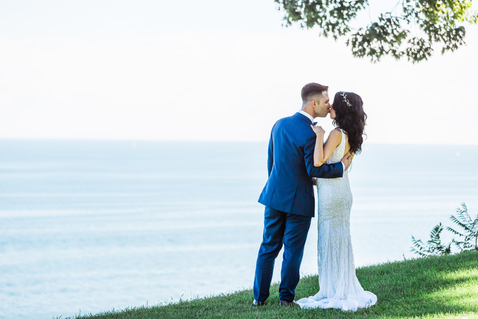 Bride and groom kiss in front of Lake Ontario waterfront at Toronto Hunt Club